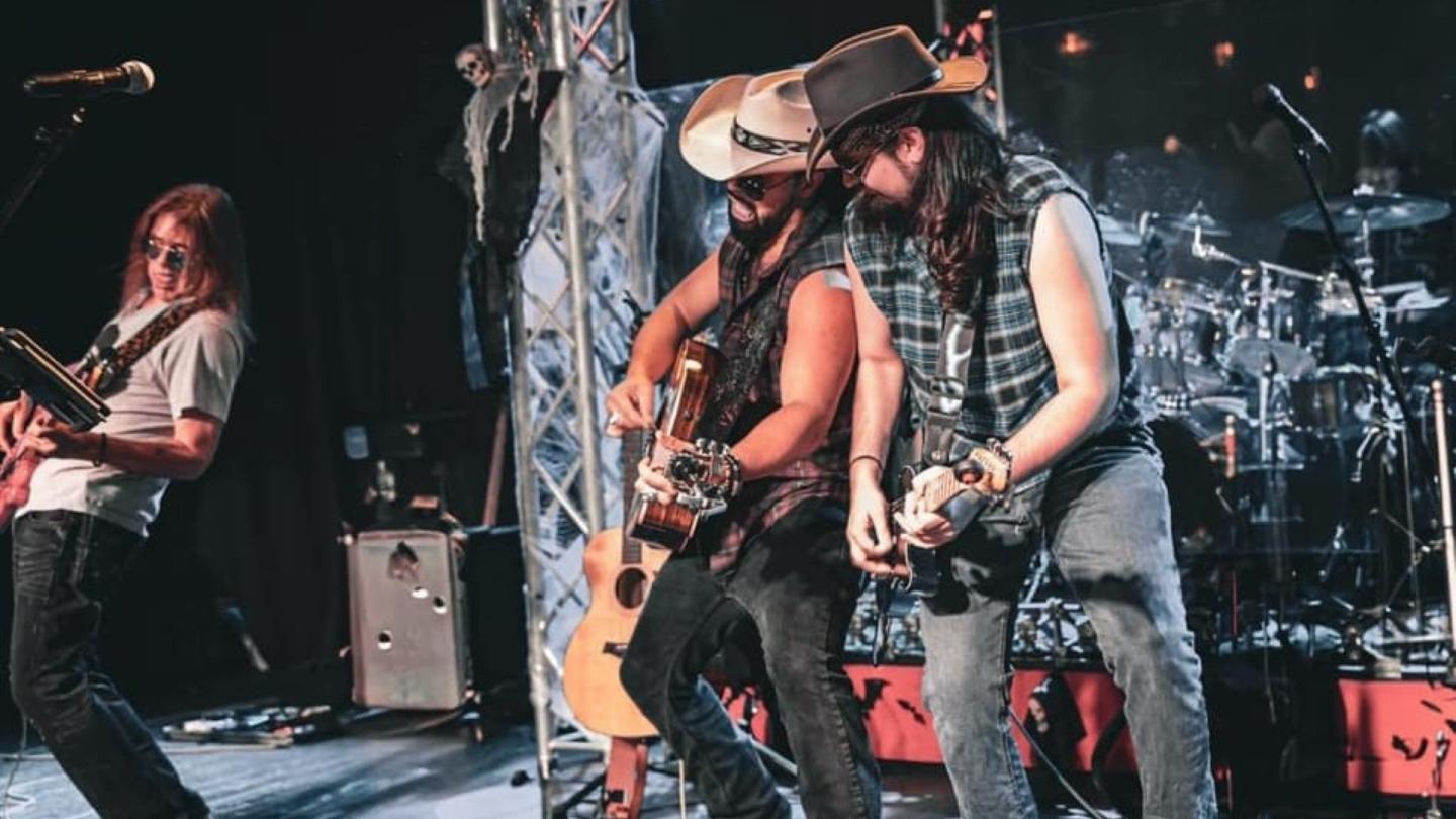 Kirk Basquez y Los Naughty Boys perform live on stage, with multiple guitarists playing under stage lights.